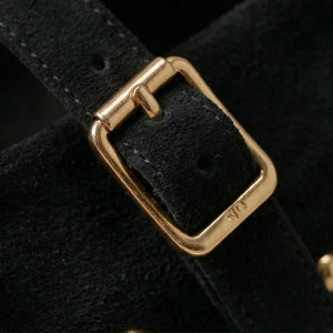 Close-up of a black leather strap with a gold buckle on a dark background