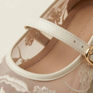 Close-up of a sandal with a white strap and gold buckle on a beige background.