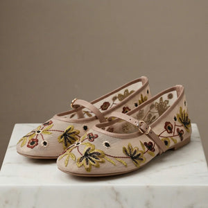 Pair of pink embroidered shoes on a marble surface with a neutral background