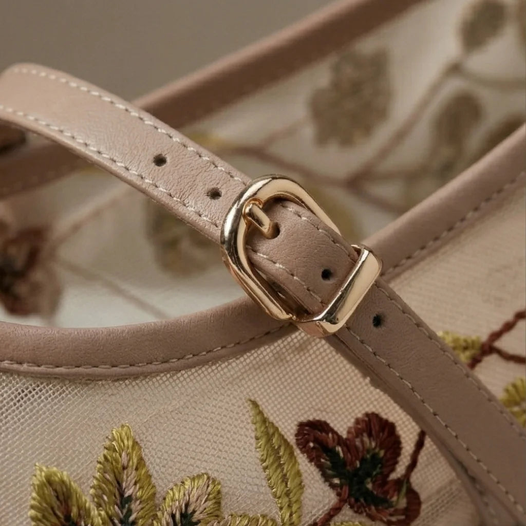 Close-up of a beige handbag with floral embroidery and a gold buckle.
