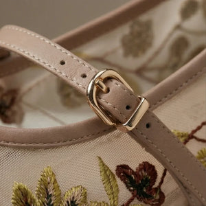 Close-up of a beige handbag with floral embroidery and a gold buckle.