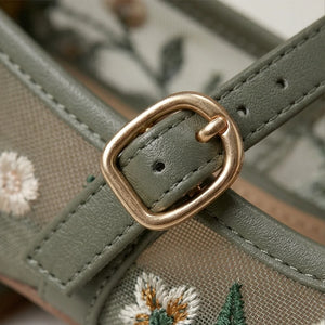 Close-up of a green handbag with floral embroidery and a gold buckle.