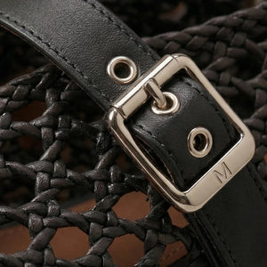 Close-up of a black woven bag with a gold buckle and 'M' logo.