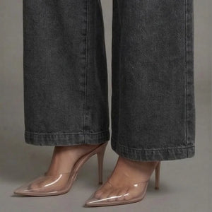 Clear high-heeled shoes worn with dark gray wide-leg jeans on a neutral background