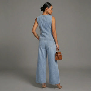 Woman wearing a denim jumpsuit holding a brown handbag against a gray background