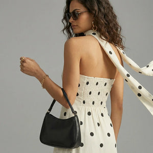 Woman in a polka dot dress holding a black handbag with a gray background