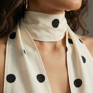White scarf with black polka dots worn around the neck, close-up view.