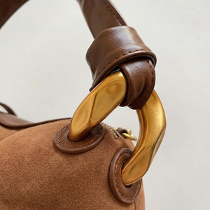 Close-up of a brown handbag with a gold handle on a light gray background
