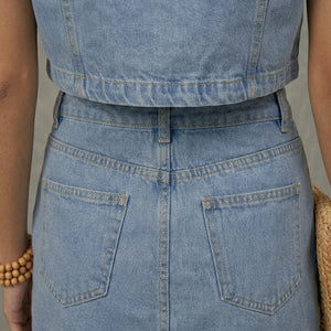Close-up of a person wearing a light blue denim apron with a neutral background