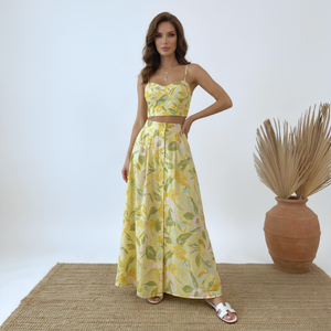 Woman wearing a yellow floral dress standing next to a vase with dried plants on a white background