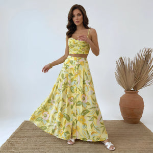 Woman wearing a yellow floral dress standing next to a vase with dried plants on a white background