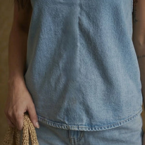 Person wearing a blue denim sleeveless top holding a woven bag.