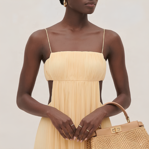 Woman wearing a beige strapless dress holding a matching handbag against a neutral background