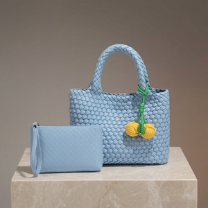 Light blue woven handbag with decorative elements on a beige surface and brown background