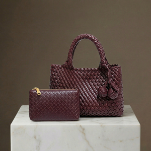 Maroon woven handbag and matching pouch on a marble surface with a brown background
