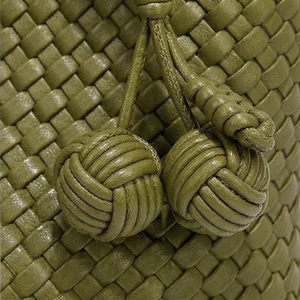 Close-up of a green woven leather bag with knotted handles.