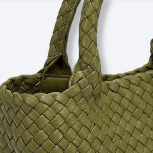 Close-up of a green woven handbag with braided handles on a white background