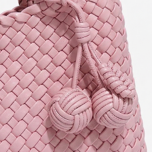 Close-up of a pink woven handbag with decorative knots on a light gray background