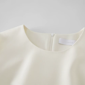 Close-up of a cream-colored garment with a brand label on a light gray background