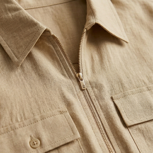 Close-up of a beige jacket with a zipper and button details.