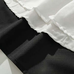 Close-up of black pants with white ruffled trim on a light background