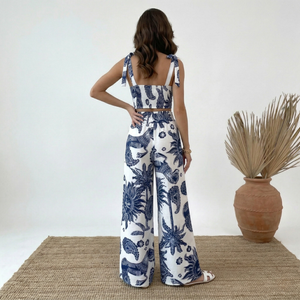 Woman wearing a blue and white floral outfit standing on a textured surface with a plant in the background.