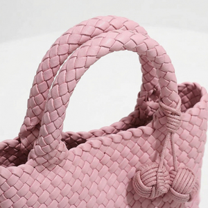 Close-up of a pink woven handbag with a decorative knot on a white background