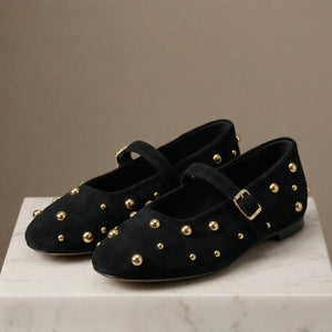 Black suede shoes with gold studs and buckles on a marble surface with a beige background