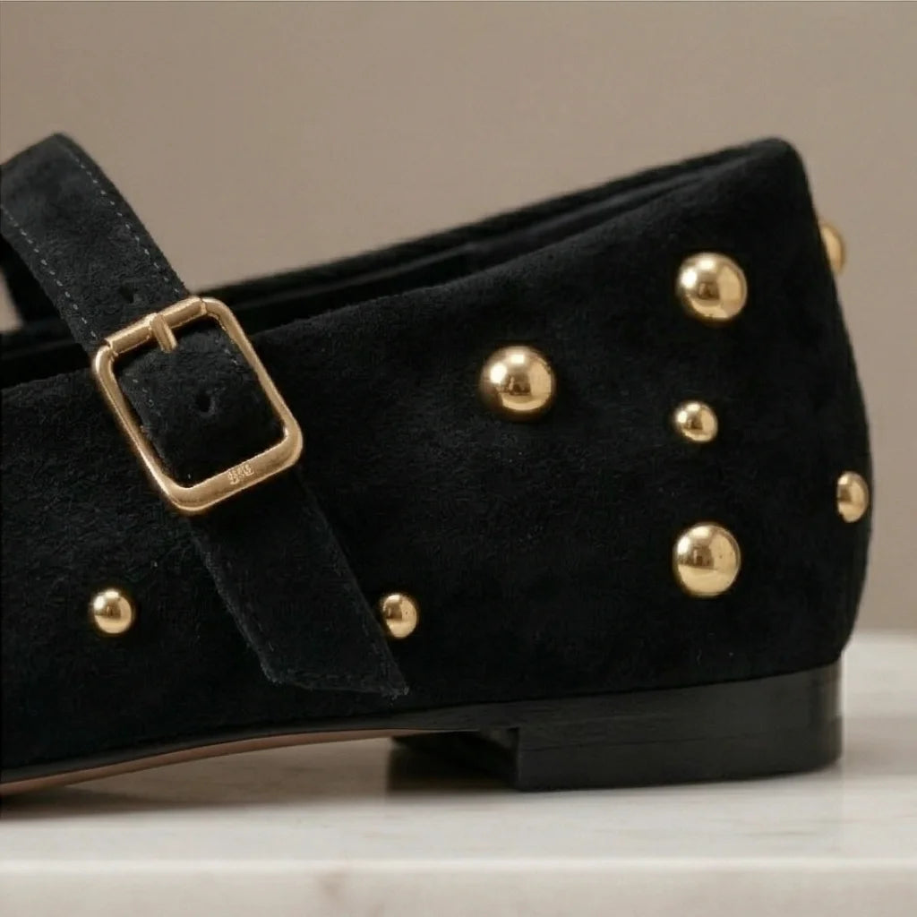 Black shoe with gold studs and buckle on a neutral background