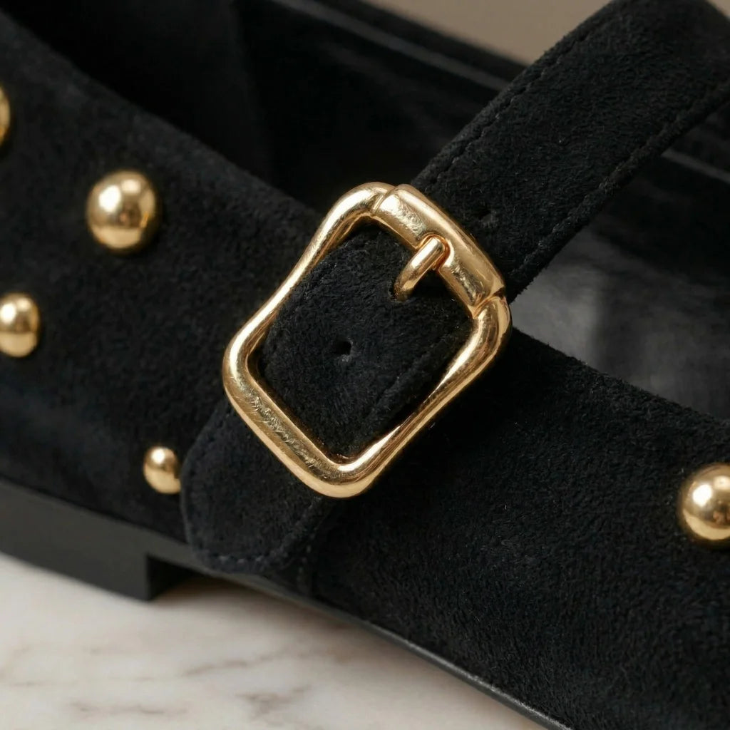 Black shoe with gold buckle and studs on a marble surface
