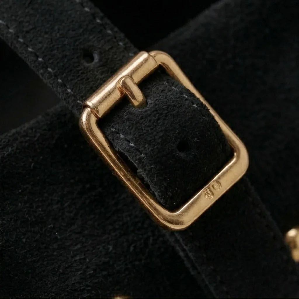 Close-up of a black leather strap with a gold buckle on a dark background