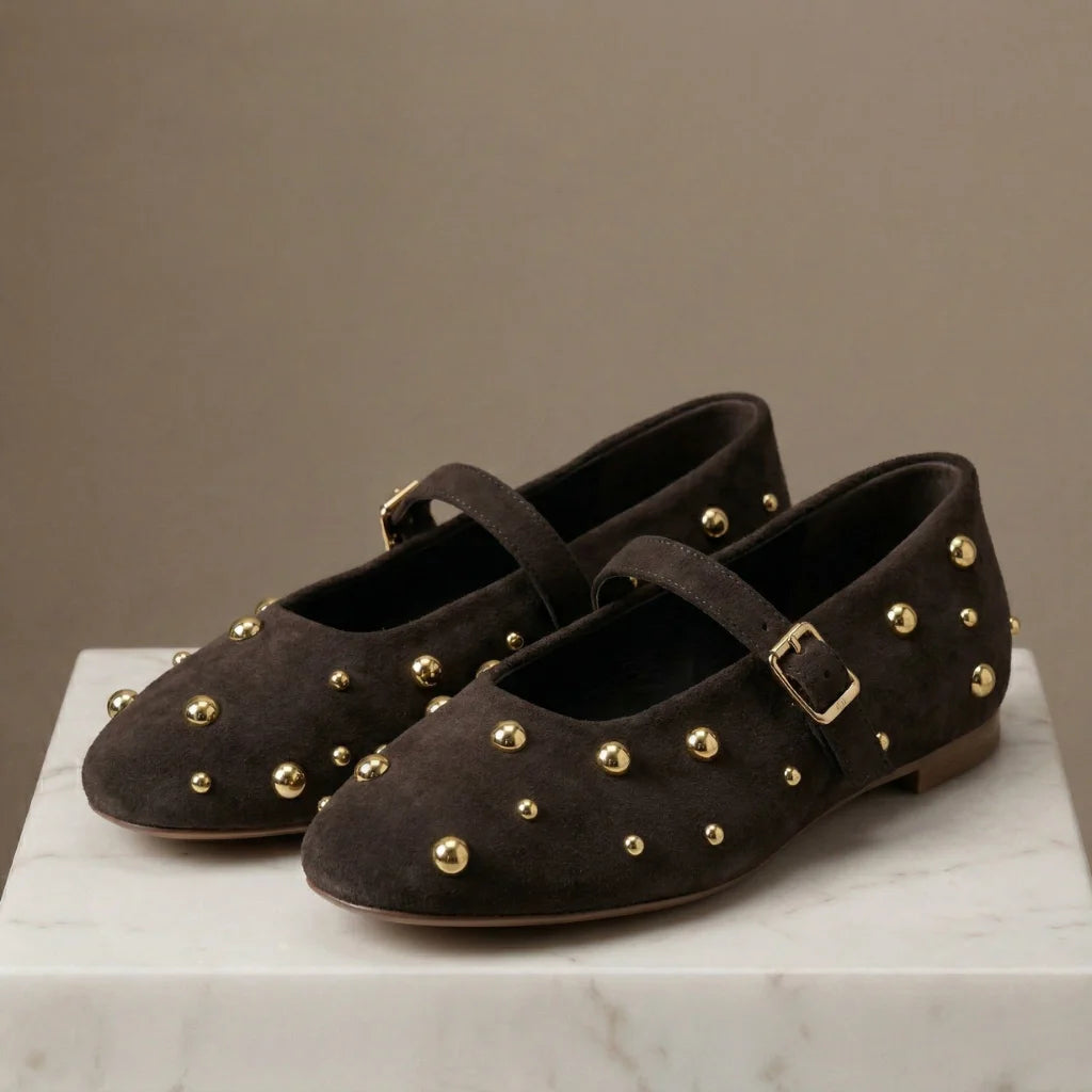 Pair of brown suede shoes with gold studs on a marble surface against a beige background