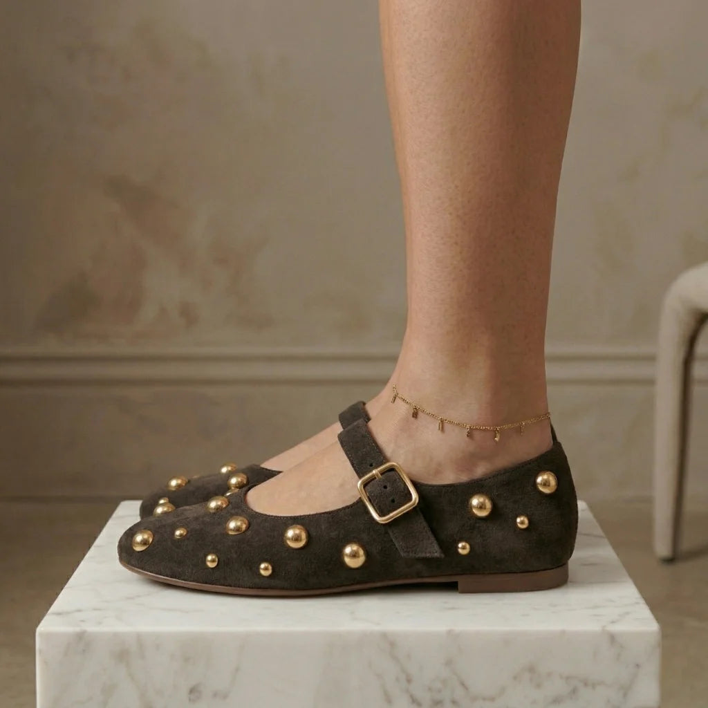 Brown studded flats worn by a person on a marble surface with a neutral background