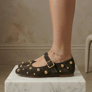 Brown studded flats worn by a person on a marble surface with a neutral background