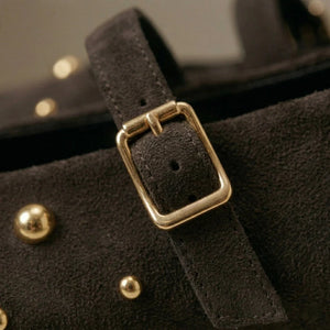 Close-up of a black leather strap with a gold buckle on a dark background