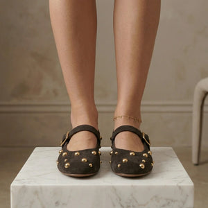 Black studded flats worn by a person on a marble surface with a neutral background