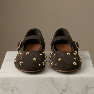 Pair of brown suede shoes with gold studs on a marble surface.