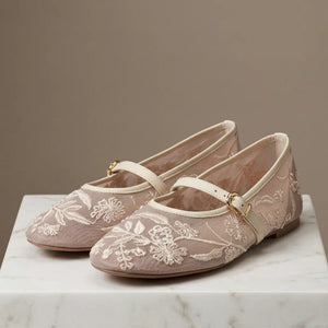 Pair of beige floral embroidered shoes on a marble surface with a neutral background