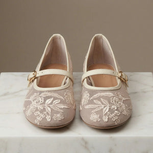 Pair of beige shoes with floral embroidery on a marble surface.