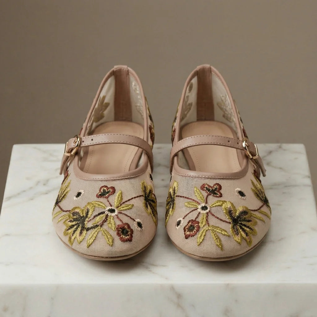 Pair of beige shoes with floral embroidery on a marble surface.