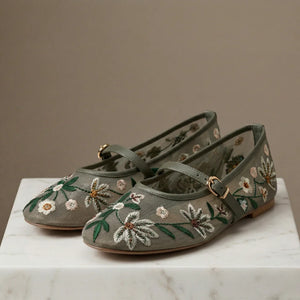 Pair of green embroidered shoes on a marble surface with a neutral background