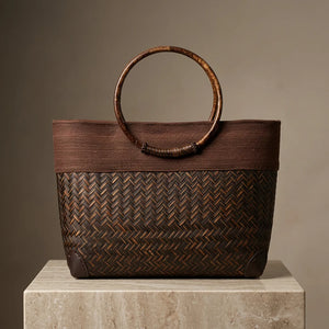 Brown woven handbag with a circular handle on a beige surface and brown background