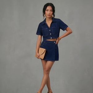 Woman wearing a denim outfit with a beige clutch against a gray background