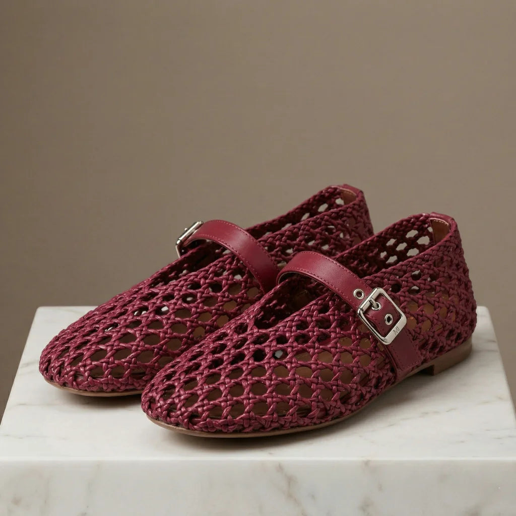 Maroon woven shoes with buckles on a marble surface against a brown background