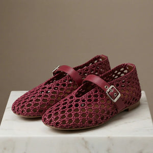 Maroon woven shoes with buckles on a marble surface against a brown background