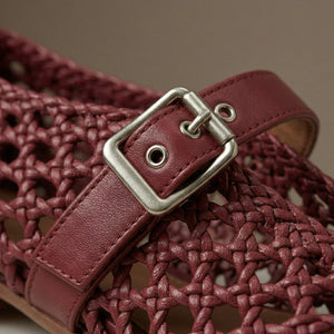 Close-up of a maroon woven sandal with a silver buckle on a neutral background