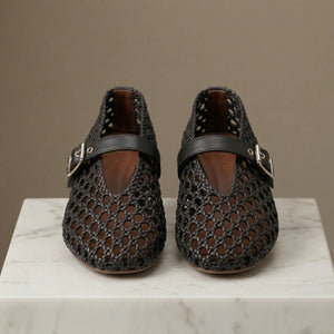 Pair of black mesh shoes with buckles on a marble surface and brown background