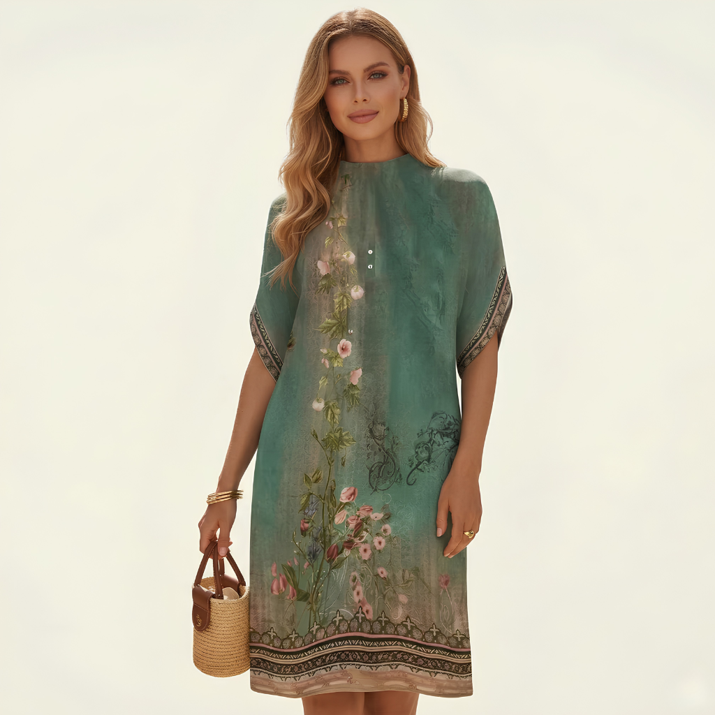 Woman wearing a teal dress with floral embroidery on a plain background