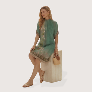 Woman in a green dress sitting on a white box with a beige handbag.