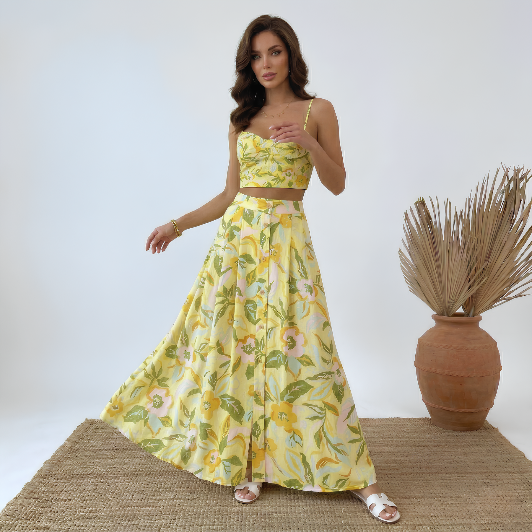 Woman wearing a yellow floral dress standing next to a vase with dried plants on a white background